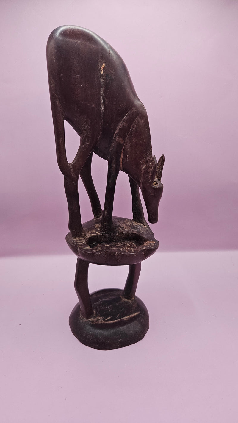 Vintage hand-carved wooden antelope sculpture, measuring 11"x3.5", featuring intricate details on a pink background.