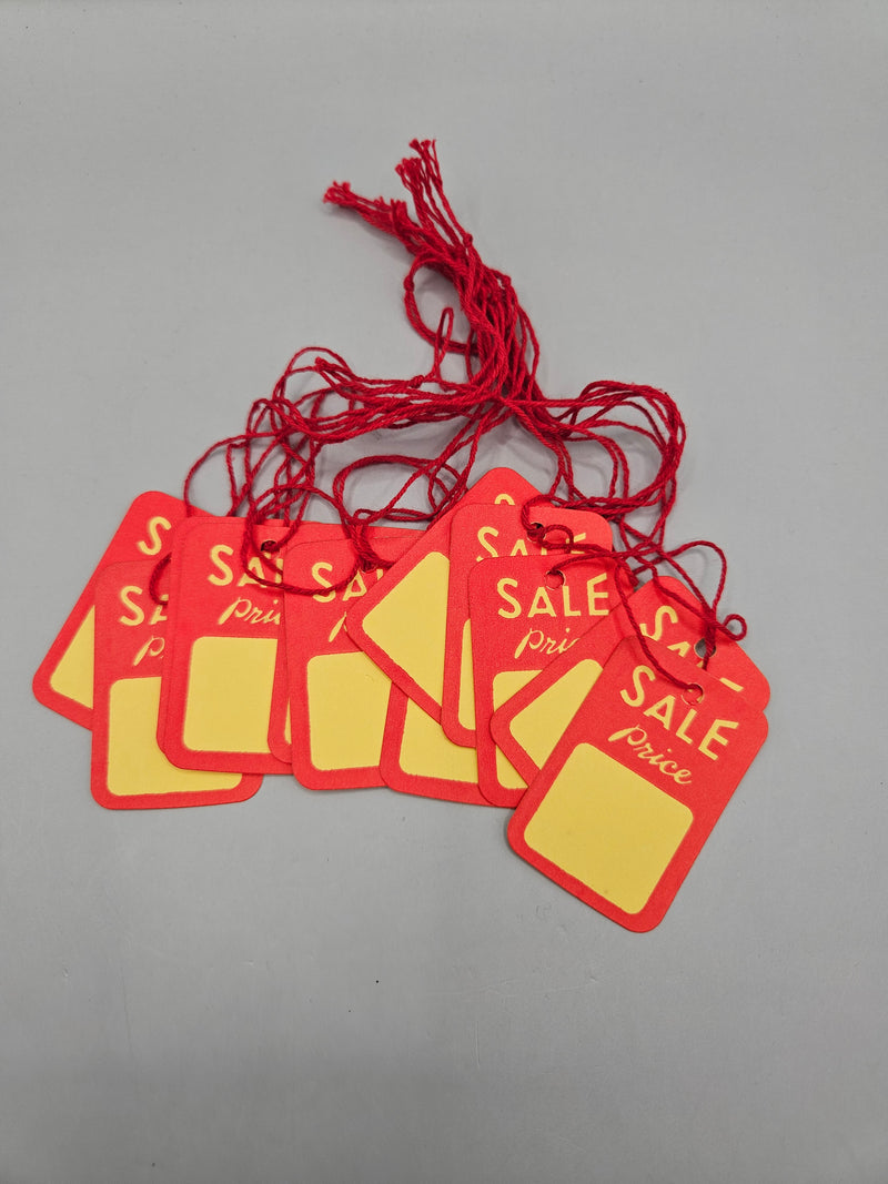 A pack of 12 vintage red and yellow sale price tags measuring 1 7/8"x1 1/4", each with a blank space for custom pricing and attached with a red string, displayed on a lined notebook.