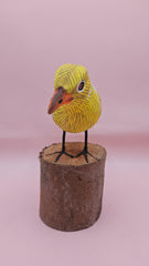 Hand-painted yellow bird figurine on wood stump with pink background – folk art decor