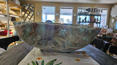 Large carved fluorite crystal bowl with green and translucent veining, displayed on tropical floral fabric