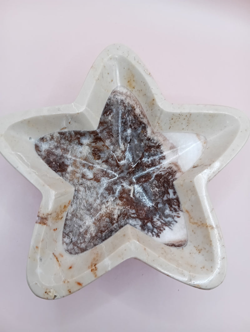 Three hand-carved onyx star bowls in brown, beige, and grey displayed vertically on a black surface