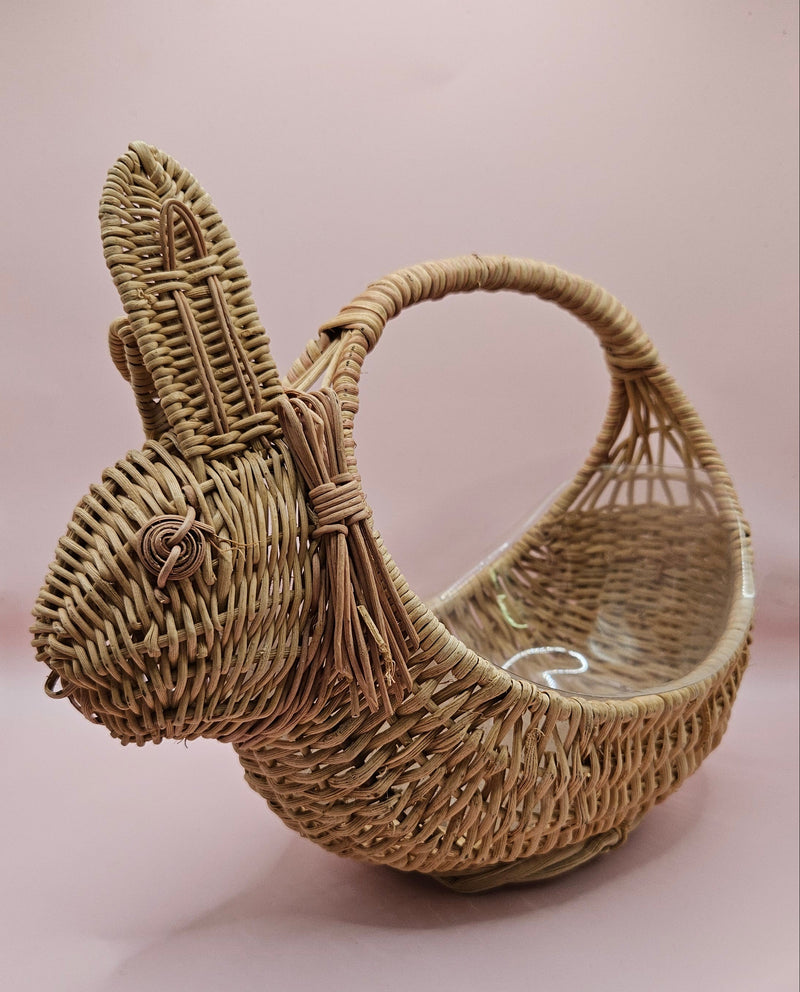Vintage handwoven wicker basket in the shape of a rabbit with detailed ears and handle, photographed against a pink background.