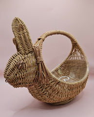 Vintage handwoven wicker basket in the shape of a rabbit with detailed ears and handle, photographed against a pink background.