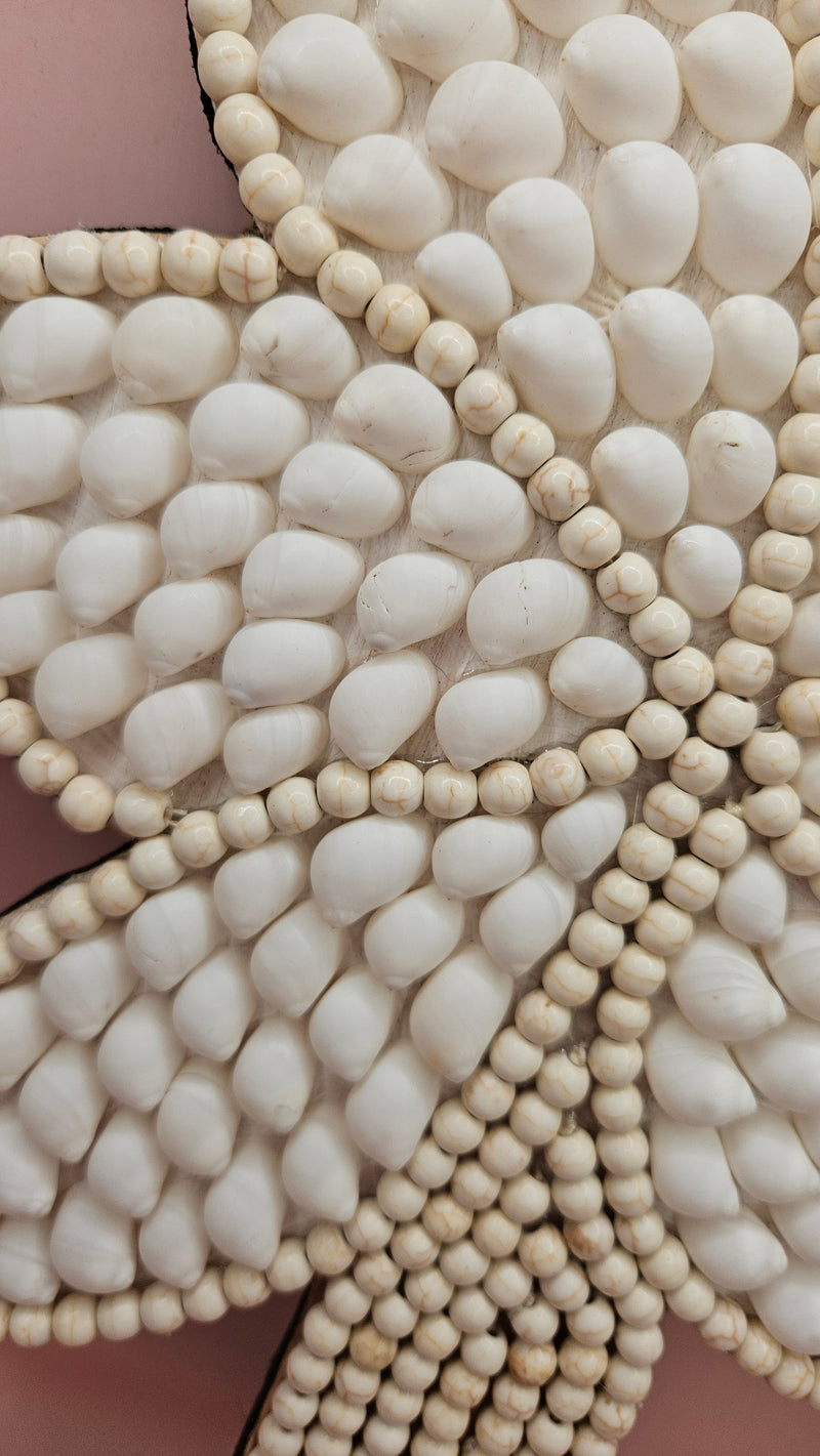 Handmade palm tree wall art made of natural white shells with beaded detailing on a pink background.