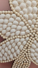 Handmade palm tree wall art made of natural white shells with beaded detailing on a pink background.