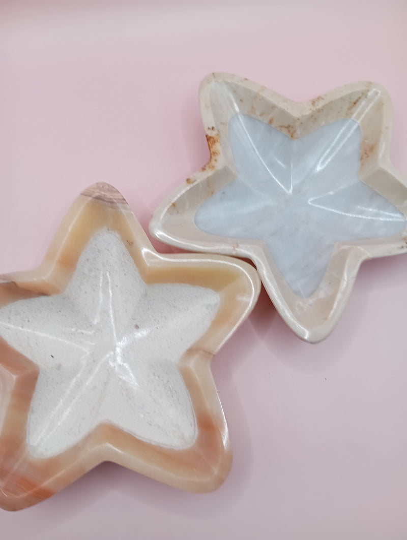 Three hand-carved onyx star bowls in brown, beige, and grey displayed vertically on a black surface
