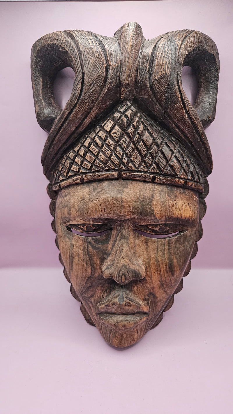 Vintage African face mask, hand-carved from wood, showcasing intricate details with natural wood grain on a pink background.