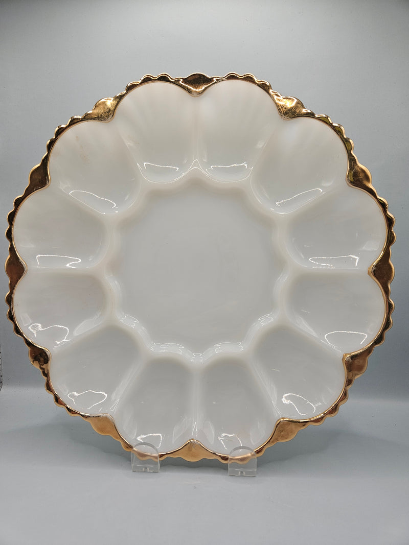 Close-up of a vintage Anchor Hocking milk glass egg holder with a gold rim, showing its elegant 10" diameter design. The plate features individual egg slots and a sophisticated gold-trimmed edge