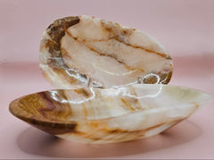 Two earth-tone onyx dishes with natural swirls of tan, cream, and rust on pink background