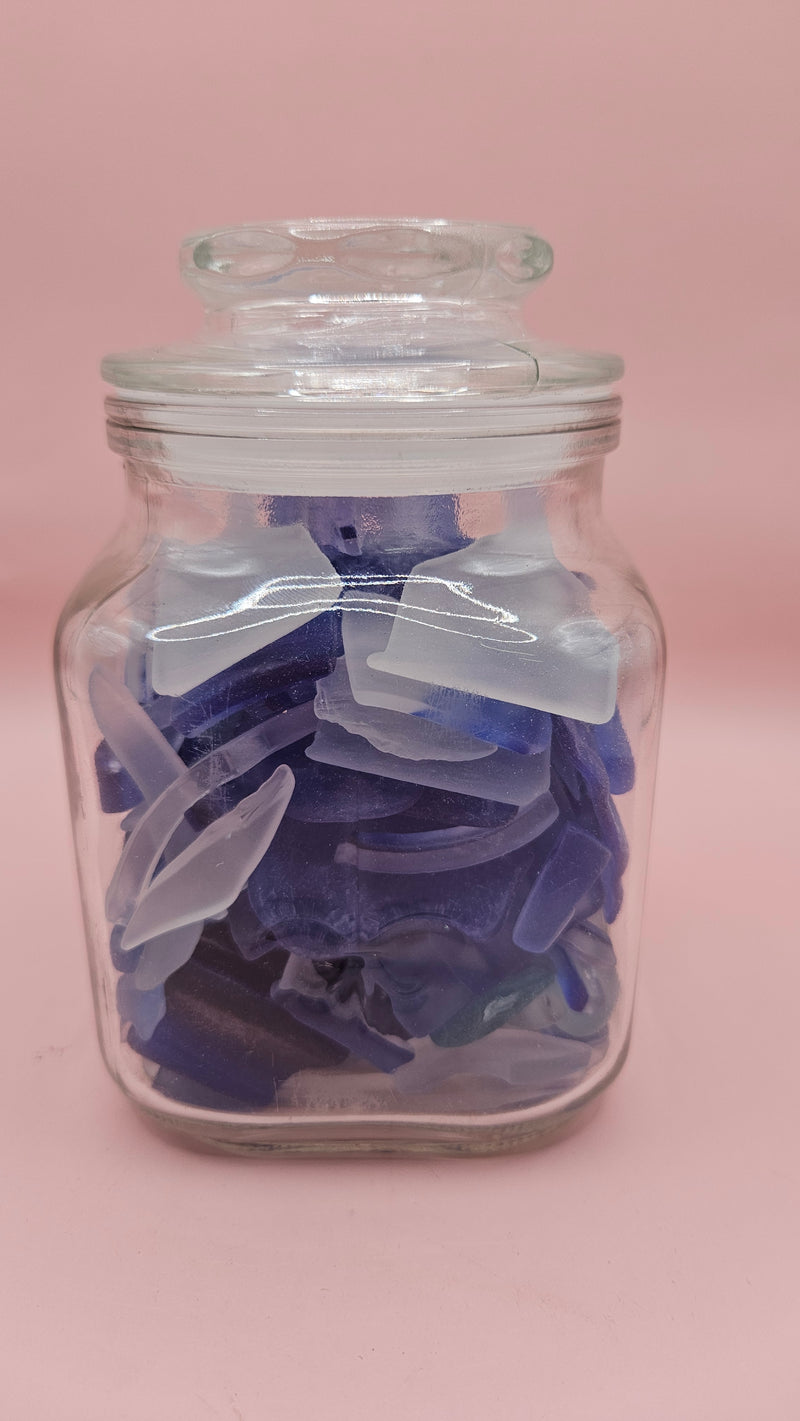 Vintage glass jar with cobalt and frosted sea glass, floral lid detail, ocean-inspired coastal decor on pink background