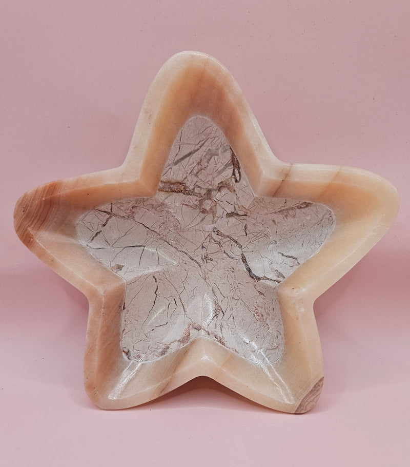 Light pink and ivory polished onyx star-shaped dish with natural veining on pink background