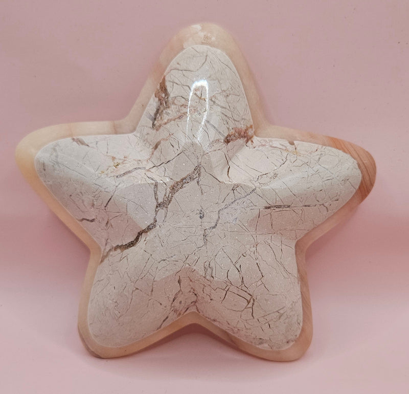 Light pink and ivory polished onyx star-shaped dish with natural veining on pink background