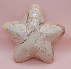 Light pink and ivory polished onyx star-shaped dish with natural veining on pink background