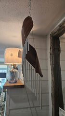 Handcrafted spiral wind chime made from natural palm frond with silver metal chimes, hanging in rustic indoor setting.