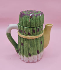 Vintage ceramic miniature teapot shaped like asparagus stalks with purple tips and a yellow ribbon bow, approximately 3.6 inches tall.