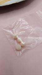 Pearl oyster shell with natural blister pearls inside and three loose pearls in a plastic bag on a pink background