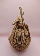Vintage handwoven wicker basket in the shape of a rabbit with detailed ears and handle, photographed against a pink background.