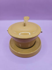 Vintage mustard yellow Descoware butter warmer with lid and trivet, cast iron design.