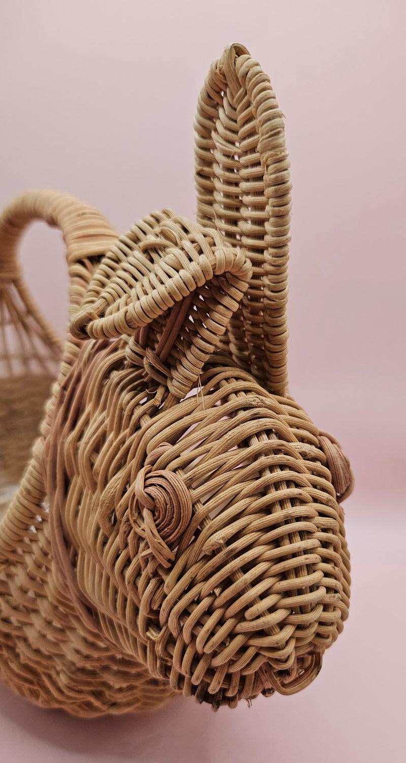 Vintage handwoven wicker basket in the shape of a rabbit with detailed ears and handle, photographed against a pink background.