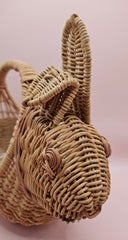 Vintage handwoven wicker basket in the shape of a rabbit with detailed ears and handle, photographed against a pink background.