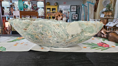Large carved fluorite crystal bowl with green and translucent veining, displayed on tropical floral fabric