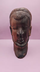 Vintage solid wood African monk sculpture, carved with detailed features, displayed against a pink background.