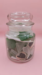 Apothecary glass jar filled with aqua and green sea glass and pottery shards, coastal decor accent on pink background