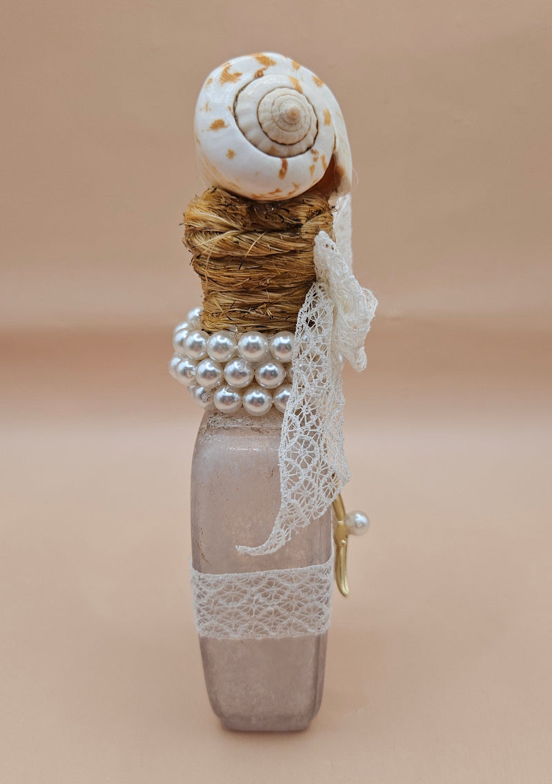 Vintage 5.5"x2" decorative bottle with a spiral seashell top, lace bow, pearl accents, and gold starfish charm against a neutral background