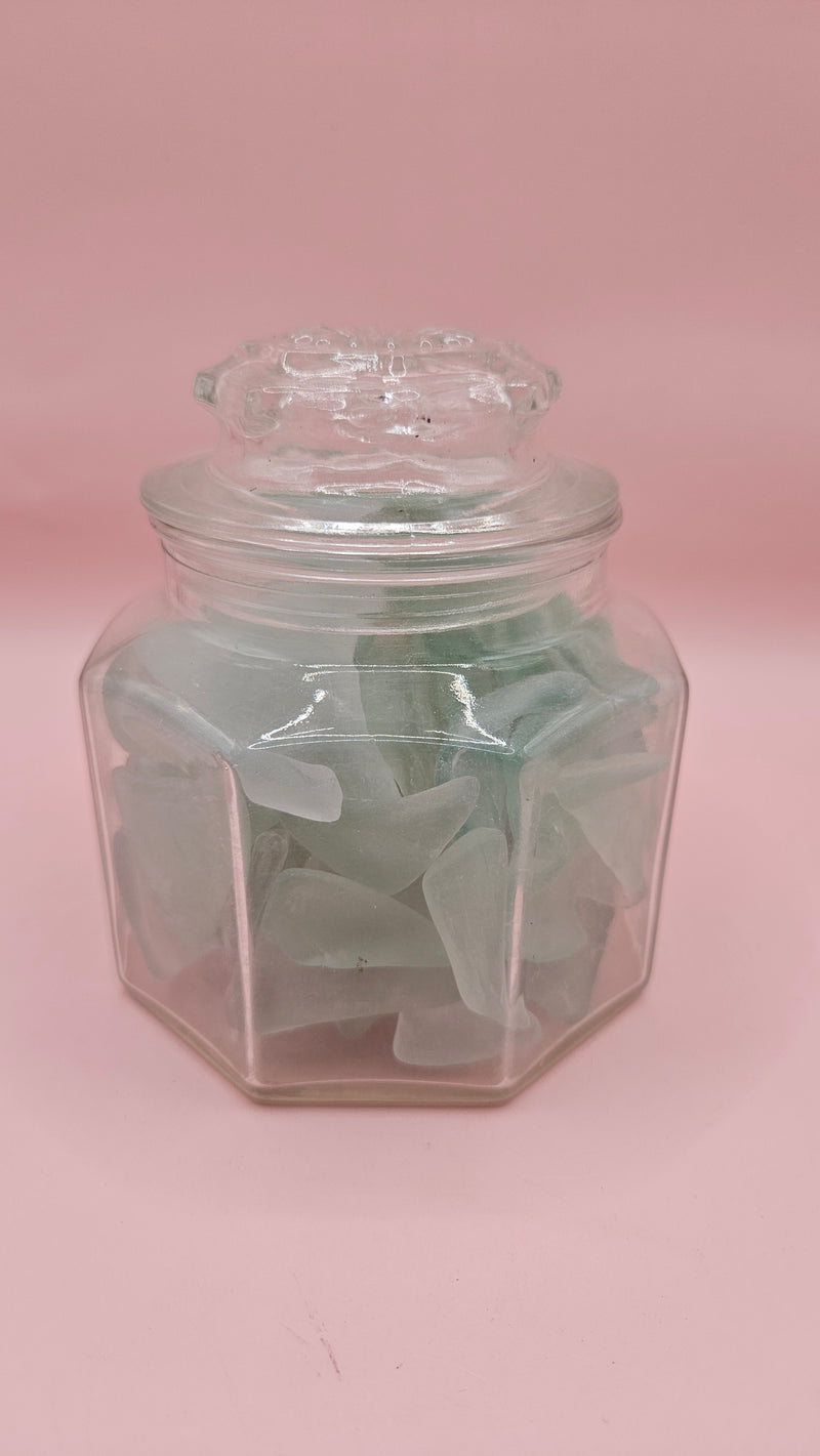 Hexagonal glass jar with lid filled with frosted aqua sea glass, coastal home decor accent on pink background