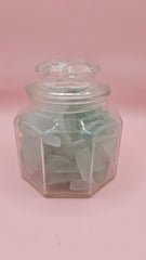 Hexagonal glass jar with lid filled with frosted aqua sea glass, coastal home decor accent on pink background