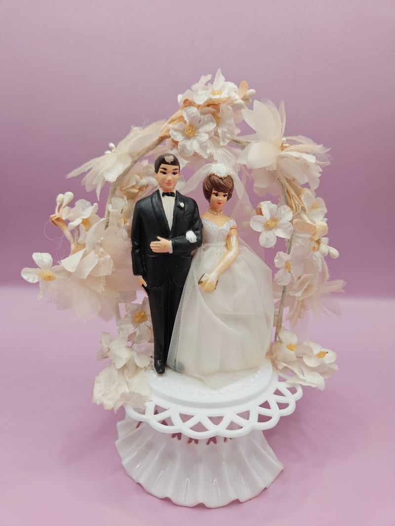 Vintage 1950s wedding cake topper with bride and groom under a floral arch, measuring 6.5 x 5 inches, slight damage to the base, perfect for retro weddings or decor