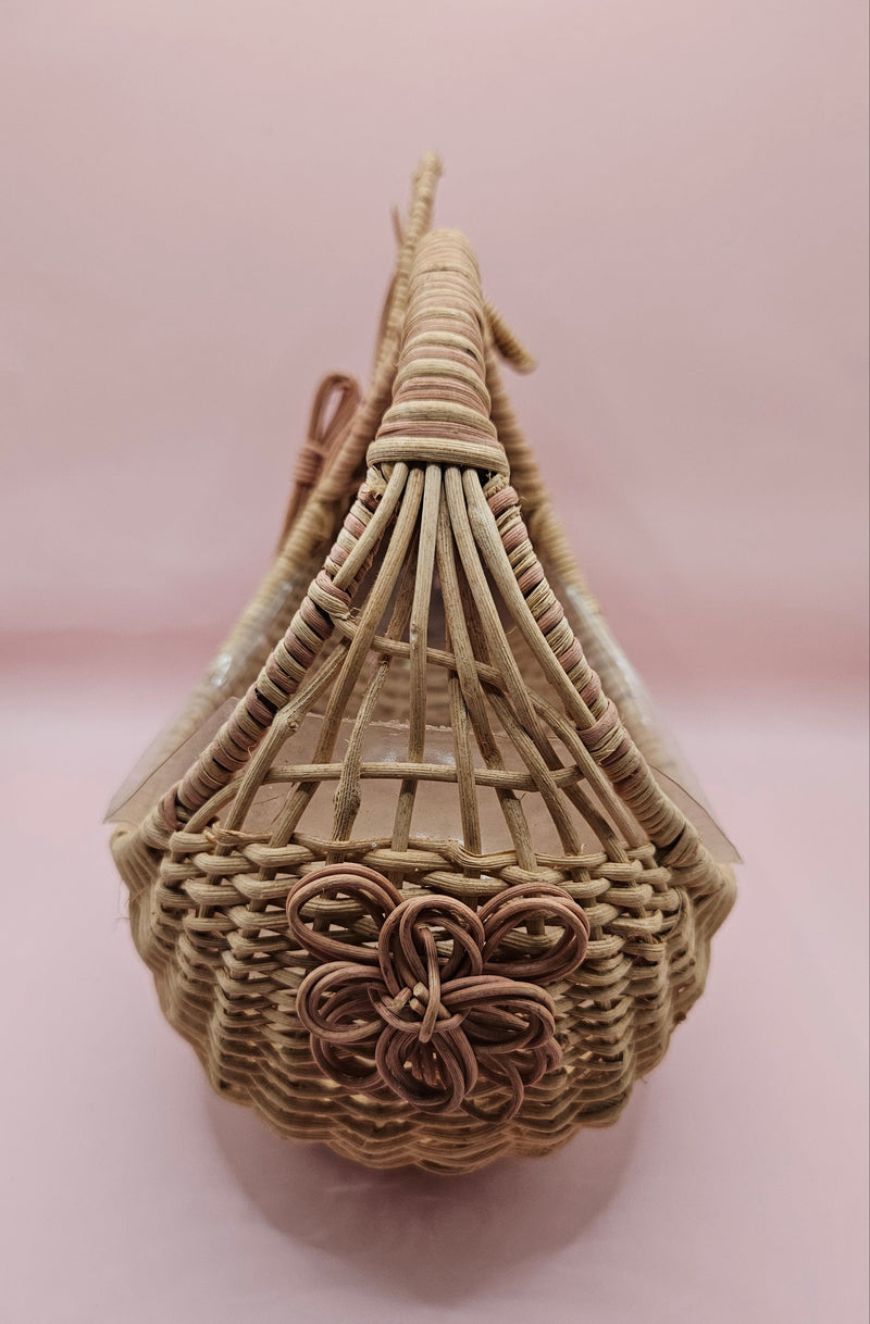Vintage handwoven wicker basket in the shape of a rabbit with detailed ears and handle, photographed against a pink background.