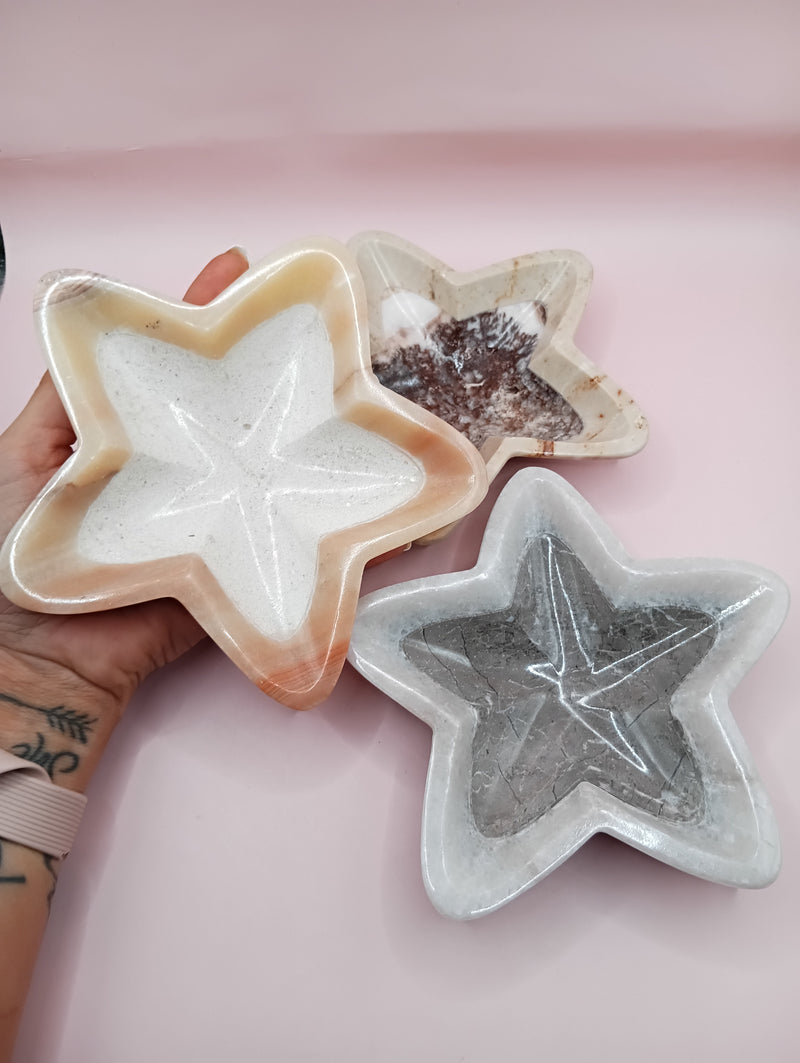 Three hand-carved onyx star bowls in brown, beige, and grey displayed vertically on a black surface