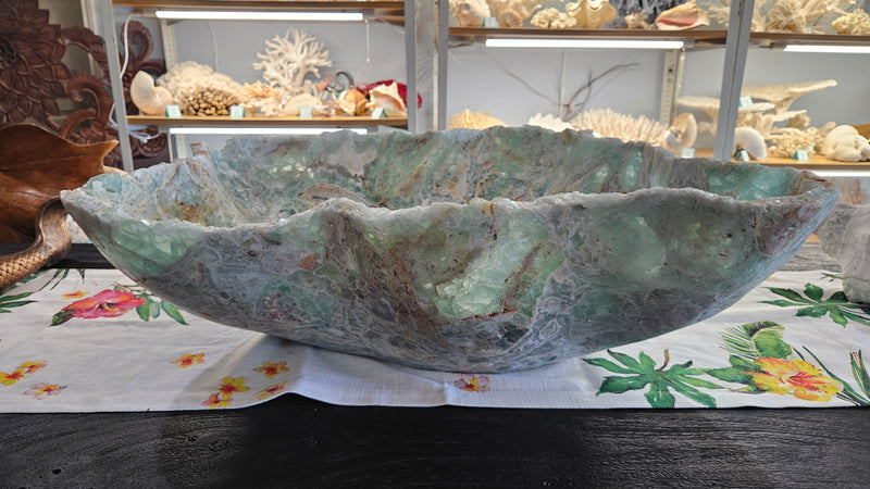 Large carved fluorite crystal bowl with green and translucent veining, displayed on tropical floral fabric