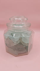 Hexagonal glass jar with lid filled with frosted aqua sea glass, coastal home decor accent on pink background