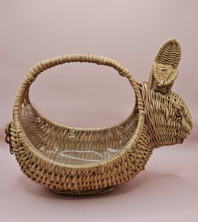 Vintage handwoven wicker basket in the shape of a rabbit with detailed ears and handle, photographed against a pink background.
