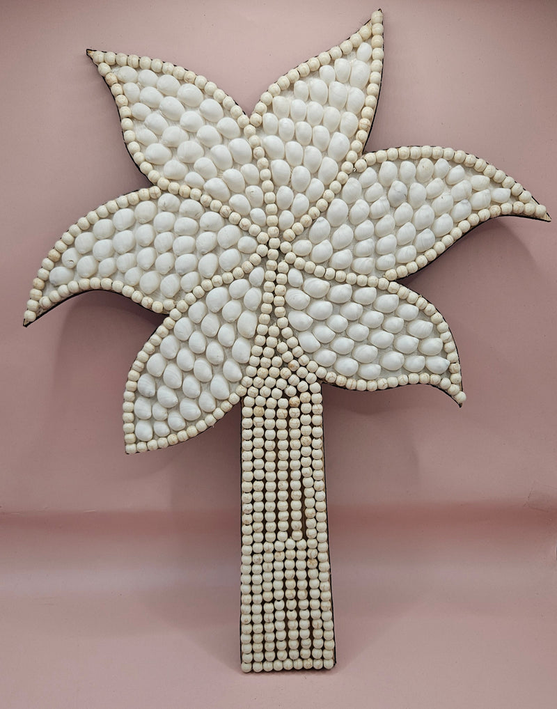 Handmade palm tree wall art made of natural white shells with beaded detailing on a pink background.