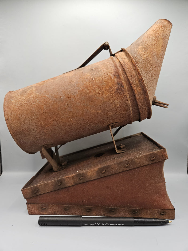 A vintage metal beekeeping smoker with a cone-shaped spout and rectangular body. The piece has a rustic, aged patina with visible rivets, making it a unique collectible or décor item for vintage and industrial-themed spaces