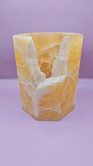 Honeycomb calcite candle cover with translucent golden tones and a hexagonal shape, measuring 6.75x5.5 inches.