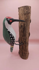 Three individual hand-painted woodpecker figures mounted on varying pieces of natural wood displayed on a teal tabletop.
