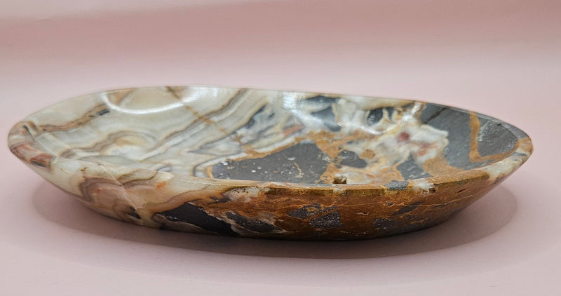 Polished onyx dish with bold black, rust, and cream patterns displayed upright on pink background