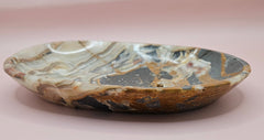 Polished onyx dish with bold black, rust, and cream patterns displayed upright on pink background