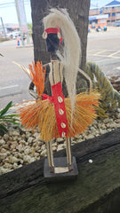 Handcrafted African tribal doll sculpture with straw skirt, cowrie shells, and a tall headdress, mounted on a wooden base.