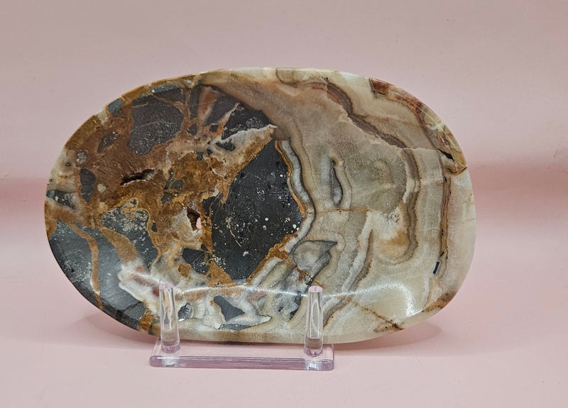Polished onyx dish with bold black, rust, and cream patterns displayed upright on pink background