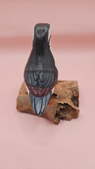 Photo of hand-carved wooden songbird figurine with grey, white, and yellow painted details, perched on a natural driftwood base.