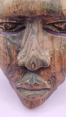 Vintage African face mask, hand-carved from wood, showcasing intricate details with natural wood grain on a pink background.