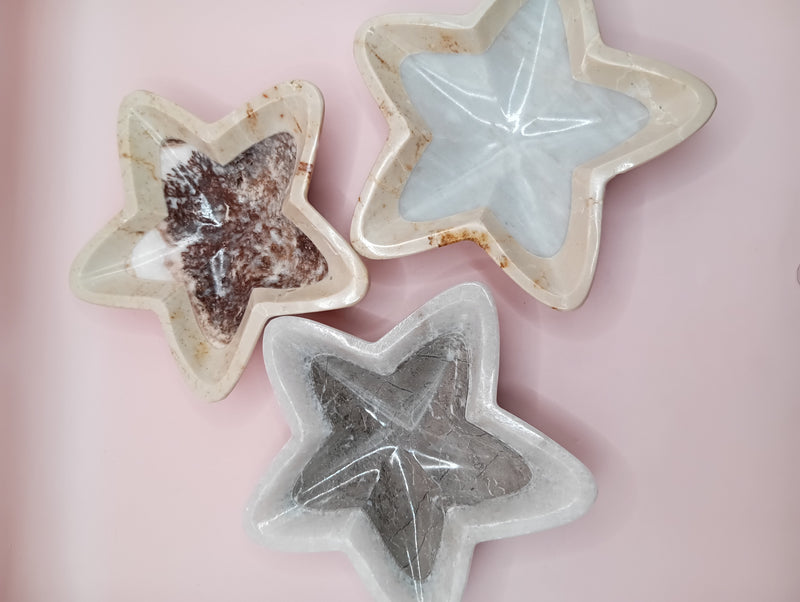 Three hand-carved onyx star bowls in brown, beige, and grey displayed vertically on a black surface