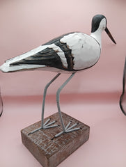 Hand-carved wooden avocet bird sculptures with black and white detailing on rustic stands