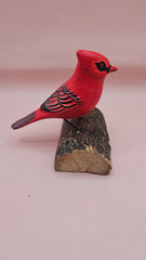 Photo of hand-carved wooden cardinal figurine, painted in bright red with black detailing, perched on a unique natural wood base.
