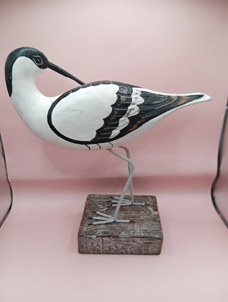 Hand-carved wooden avocet bird sculptures with black and white detailing on rustic stands